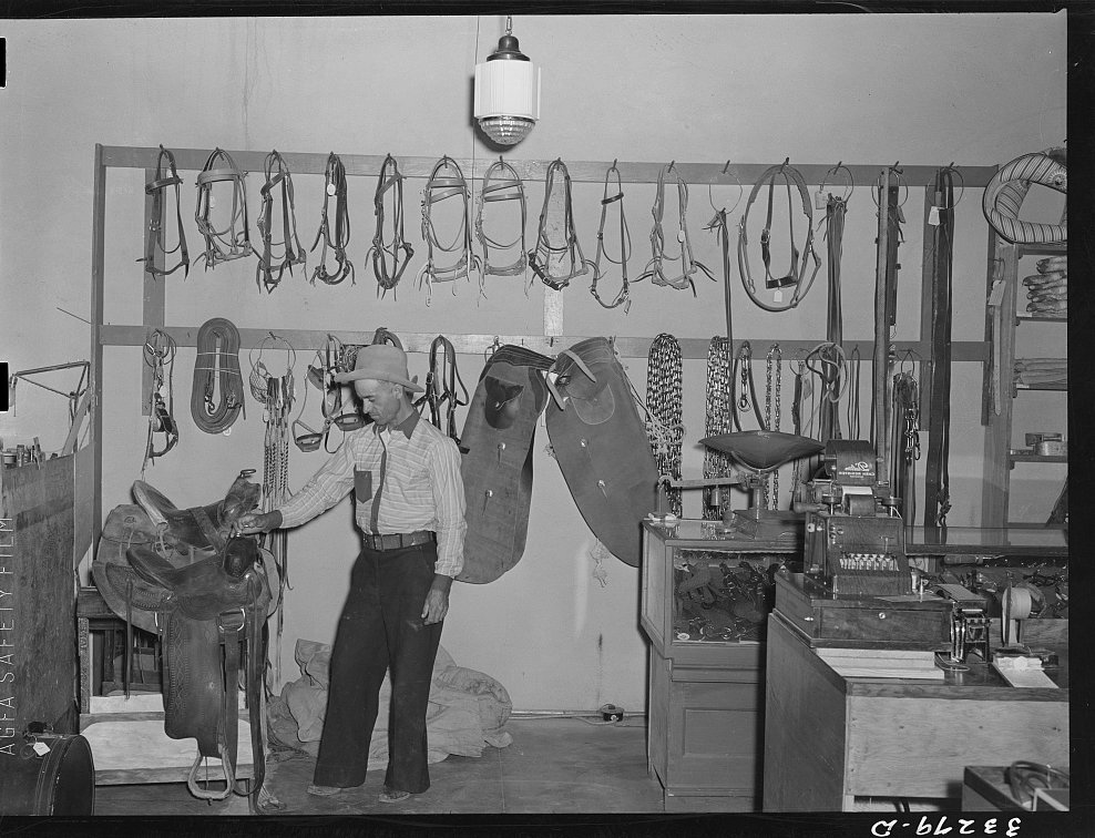 A cowboy examining a western stock saddle in a ranch supply store, Alpine, Texas, 1939